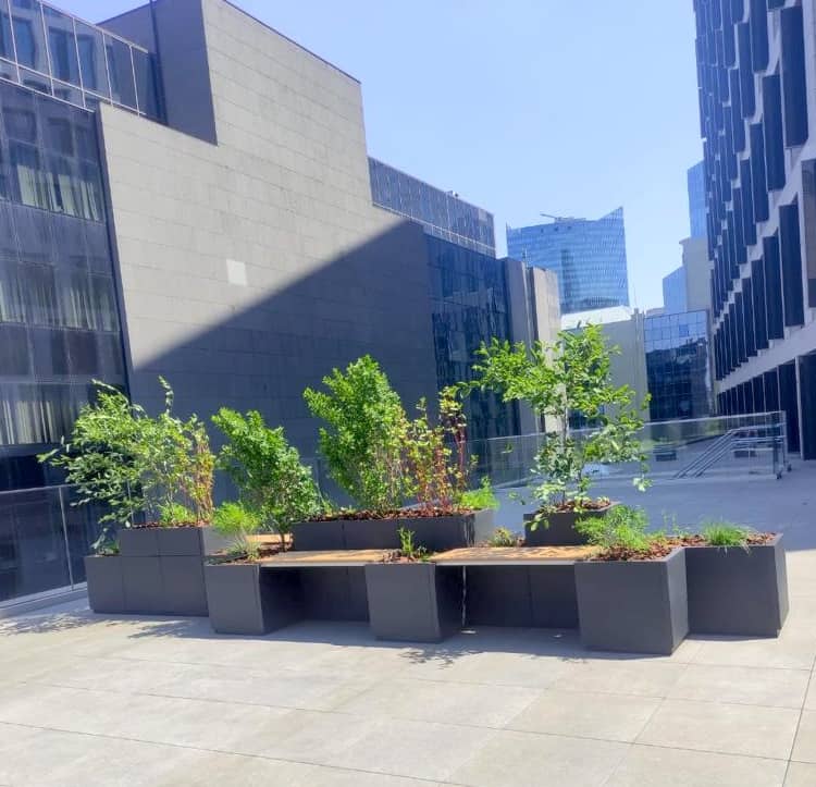 Plantenbakken in speciaal design met zitbanken zorgen voor groen accent en bakenen zones op esplanade naast modern kantoorgebouw af